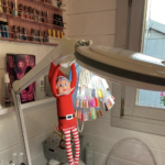 "Elf on the shelf" in the beauty cabin hanging off a light.